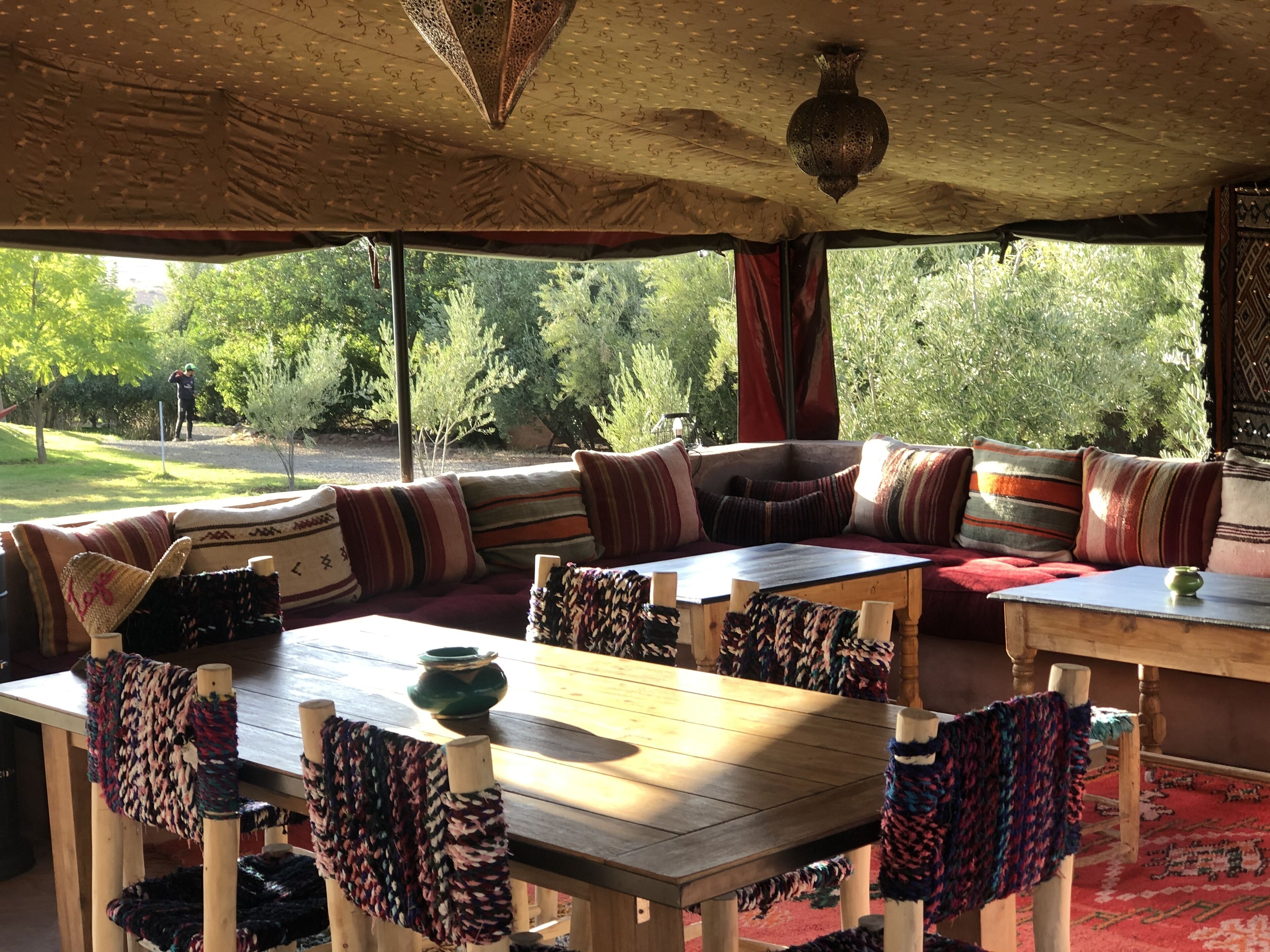 An outdoor seating area with a wooden table and chairs, a cushioned bench, and a view of a garden.