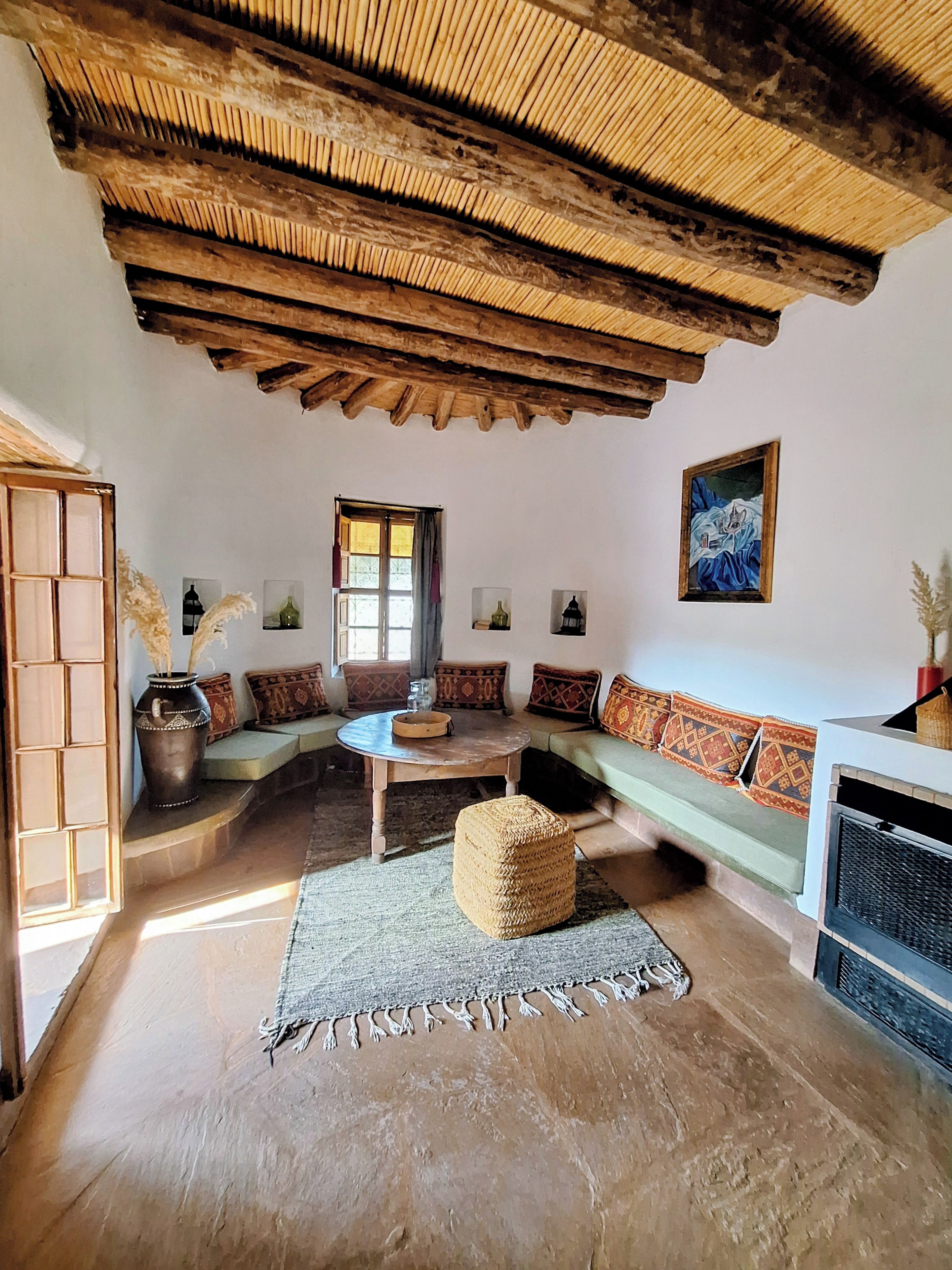 Un interior rústico con techo de madera, un conjunto de sofás, una mesa redonda y un jarrón decorativo.