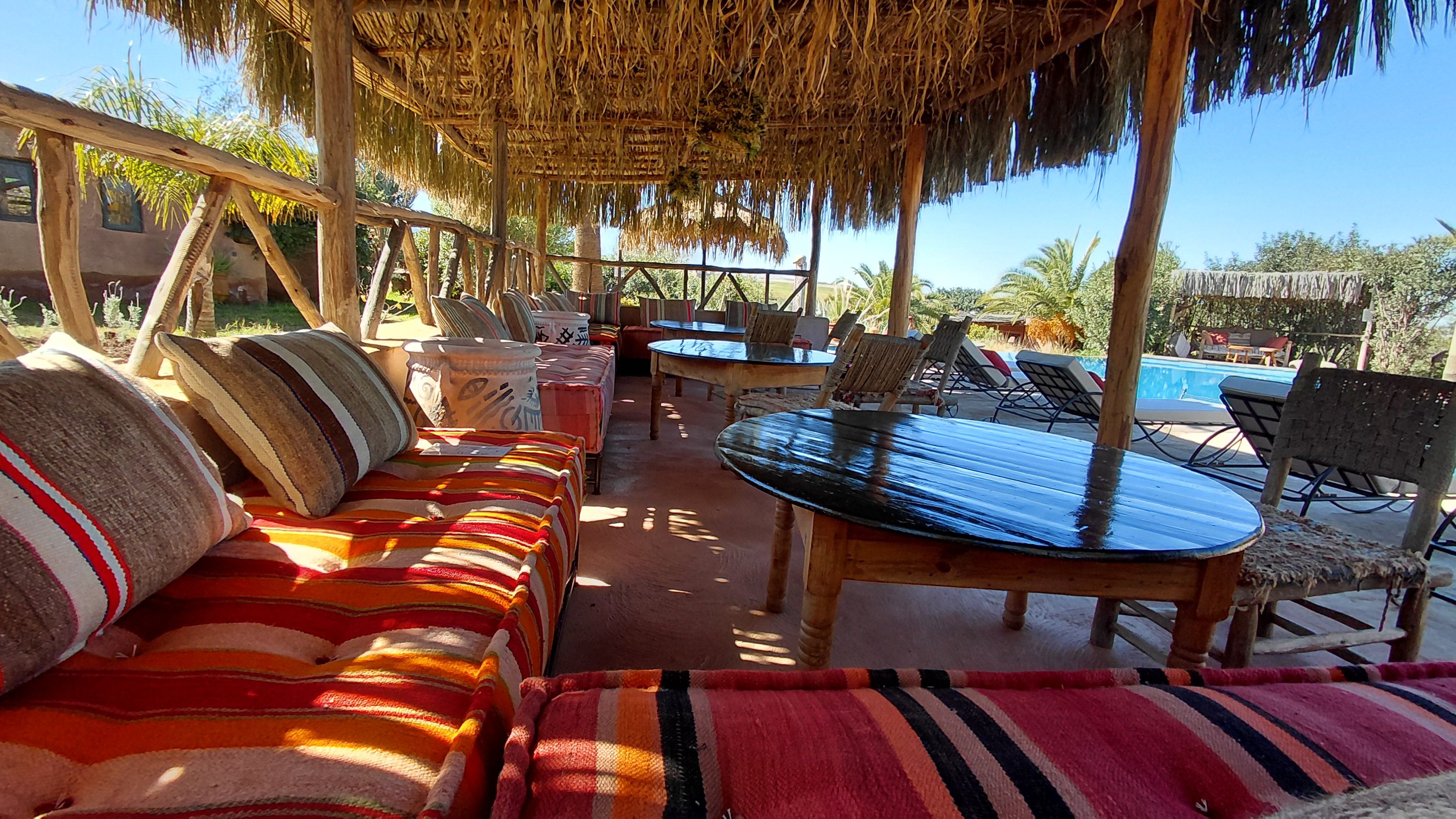 Un área de estar al aire libre con techo de paja, piscina y vistas del paisaje circundante.