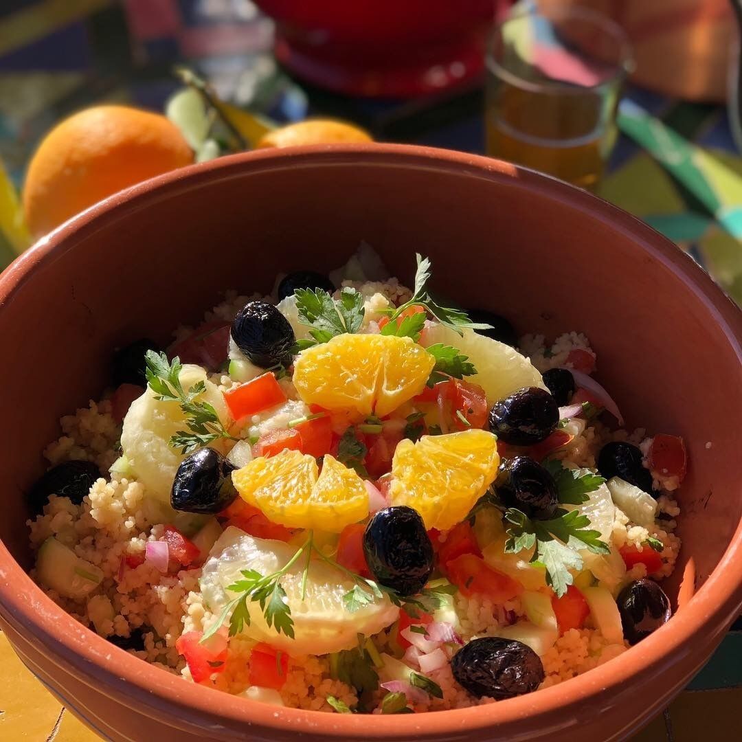A bowl of couscous salad with vegetables and olives.