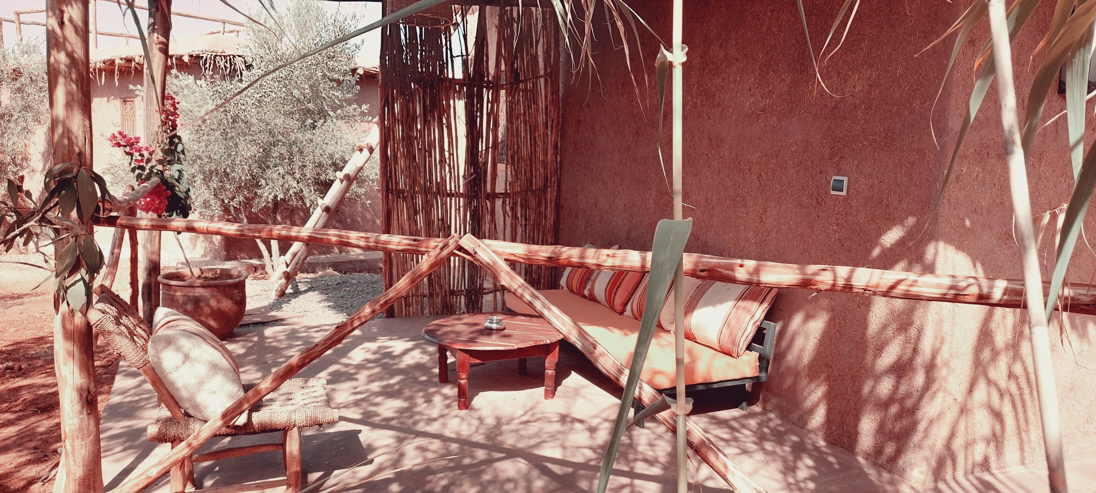 An outdoor seating area with a wooden table and chairs, surrounded by bamboo structures and a red wall.