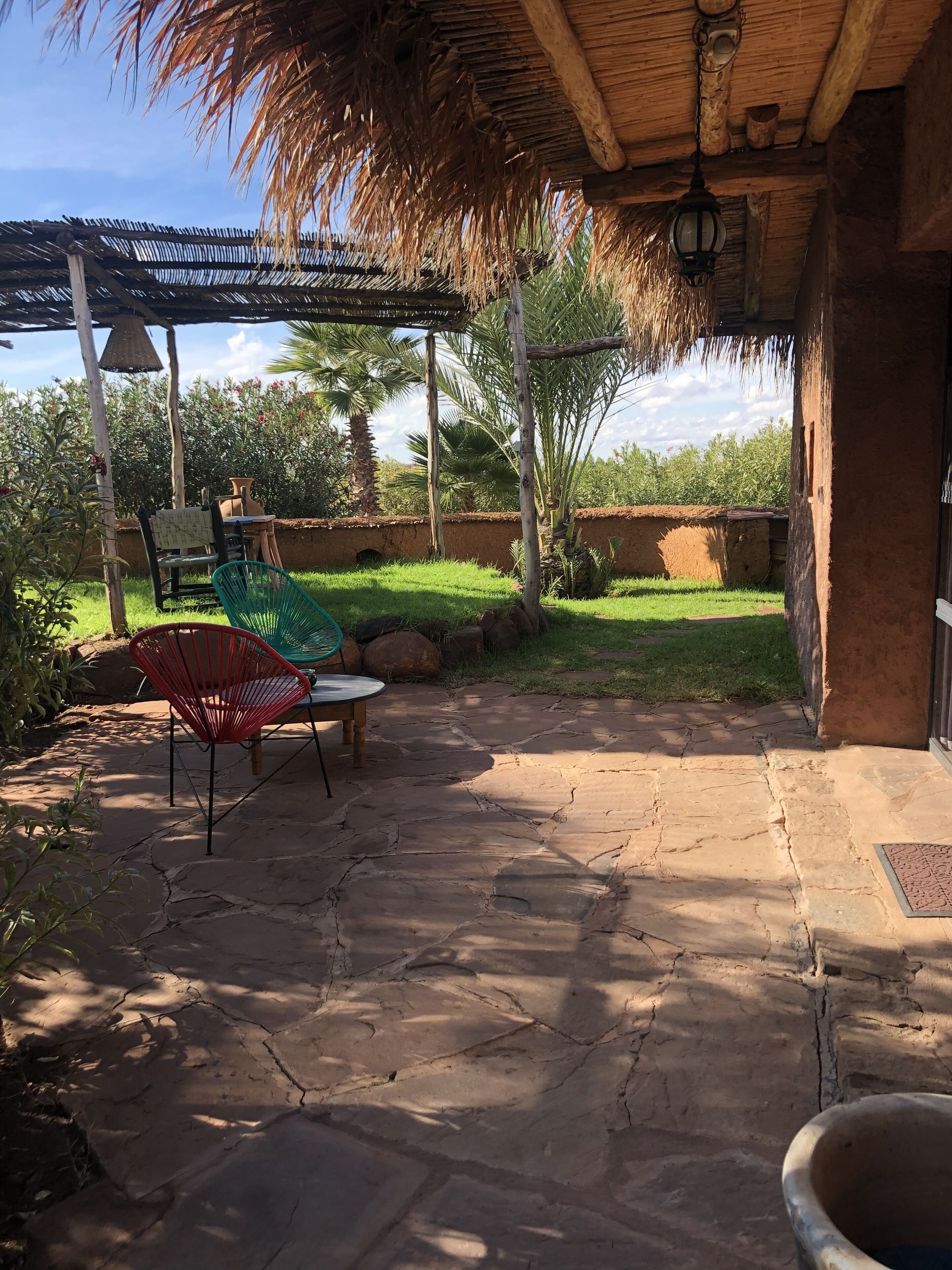 A patio area with stone flooring, a thatched roof, and a table with chairs.