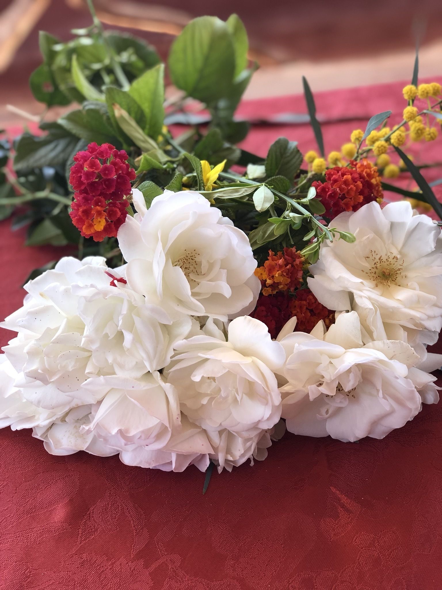 Um arranjo de flores brancas com detalhes em vermelho e amarelo, apoiado sobre uma superfície de tecido vermelho.