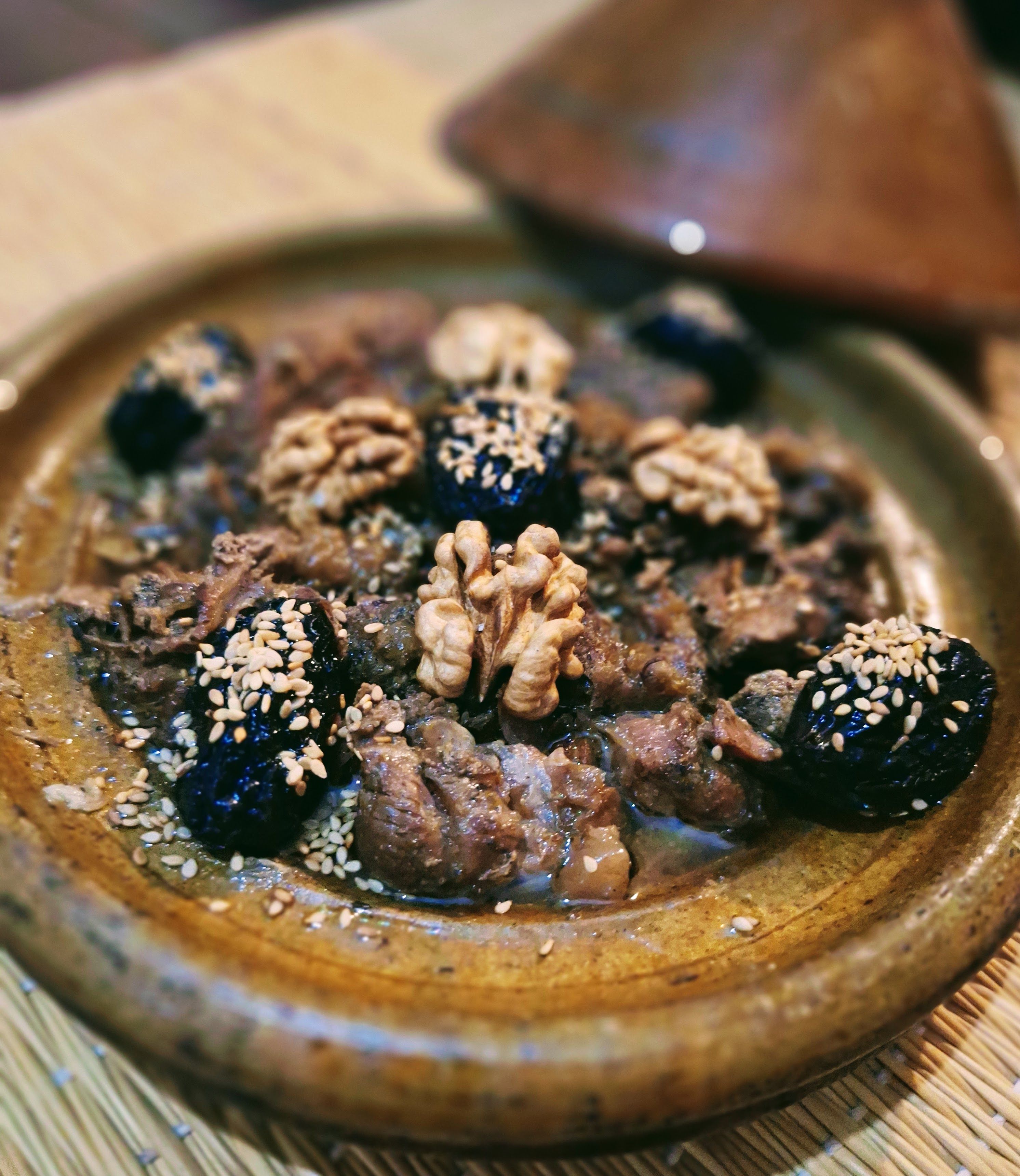 A dish with meat, walnuts, and a dark sauce, garnished with sesame seeds, served on a ceramic plate.