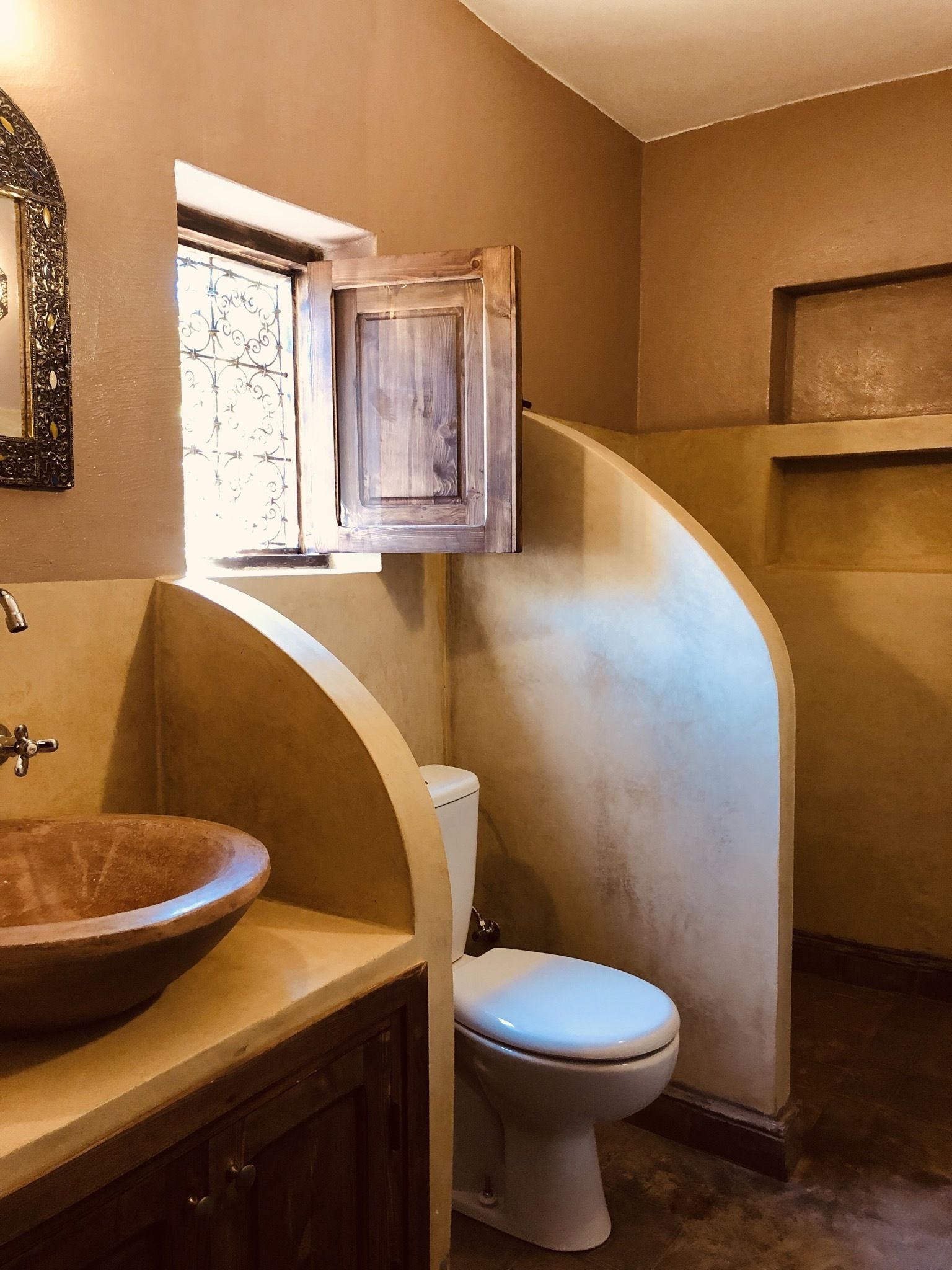 A bathroom with a wooden vanity, a white toilet, and a window with decorative iron bars.