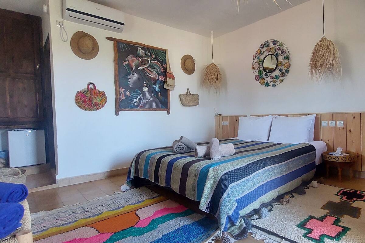 Ein Schlafzimmer mit einem Bett, einem Holzschrank, einem kleinen Tisch mit Lampe und einer Wand mit Dekorationselementen.