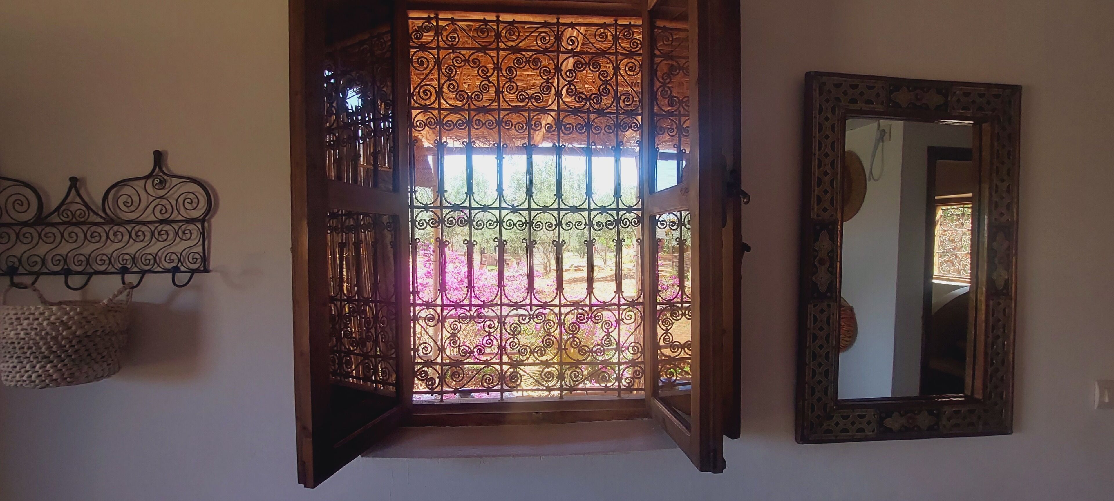 Une porte ouverte ornée de motifs métalliques complexes, un miroir accroché au mur et un panier tressé suspendu à gauche.