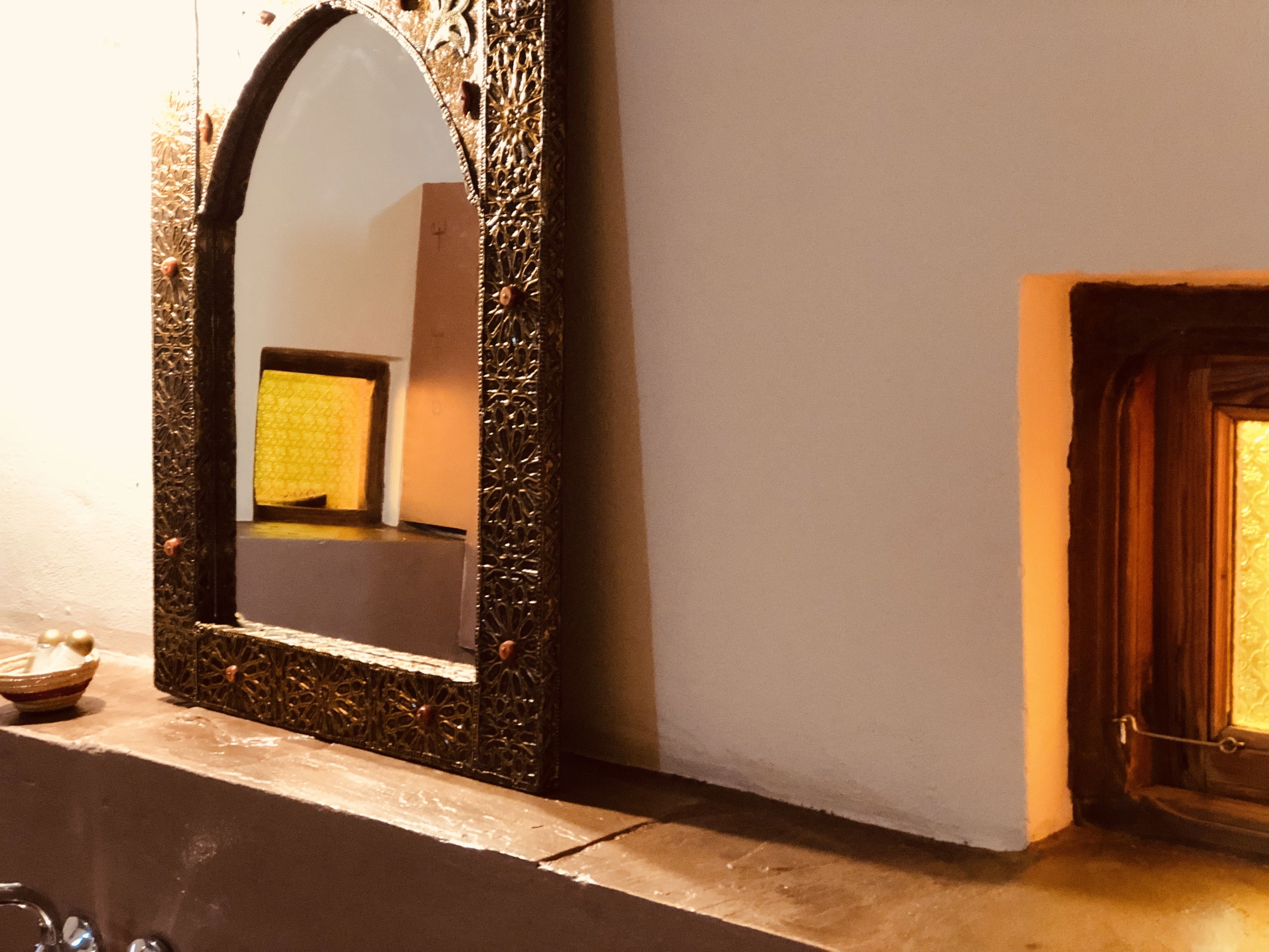 A mirror with an ornate frame, a fireplace, and a small table with a bowl and a candle.