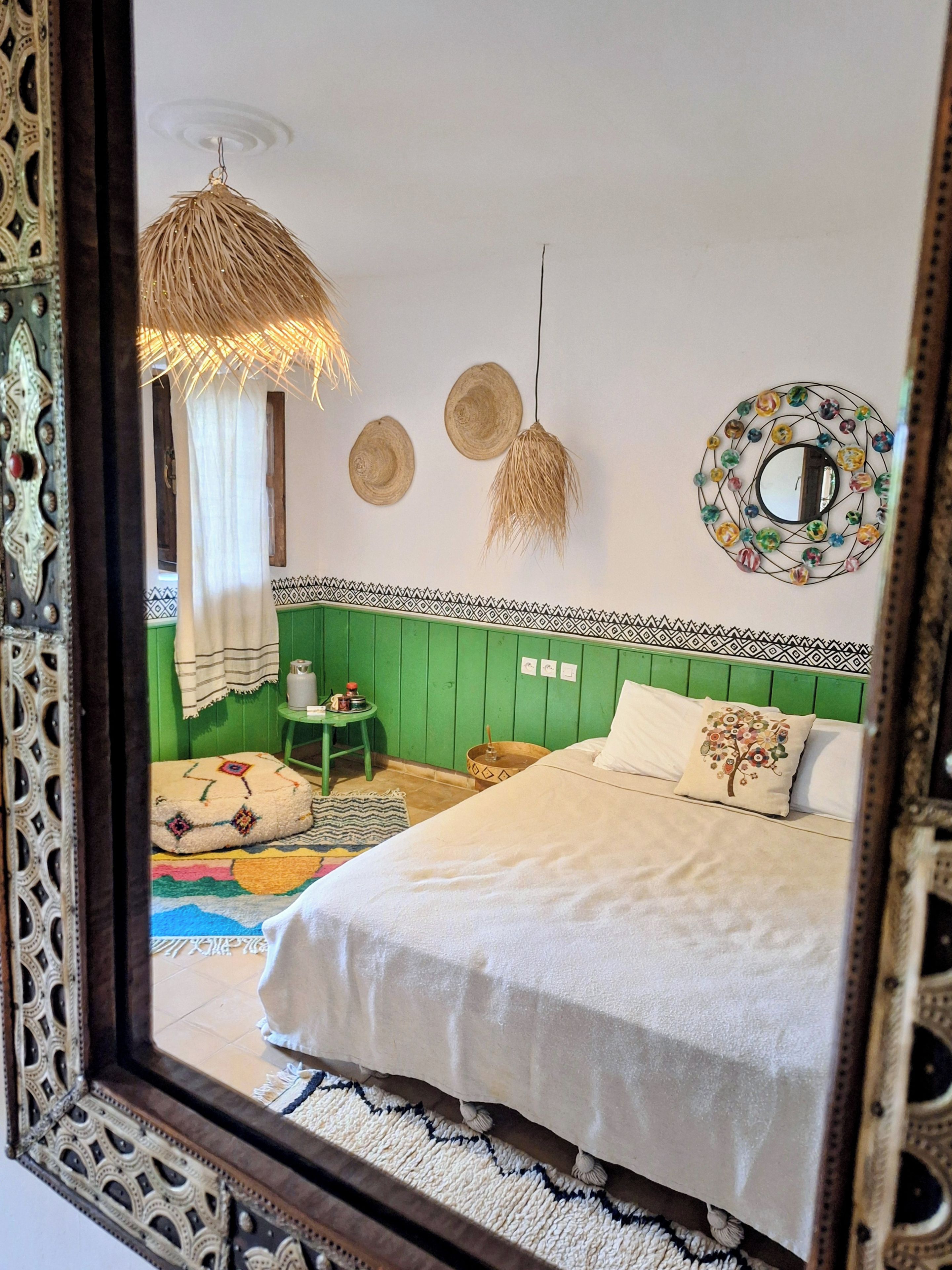 A room with a bed, a hanging light fixture, a wall-mounted mirror, and a patterned border.
