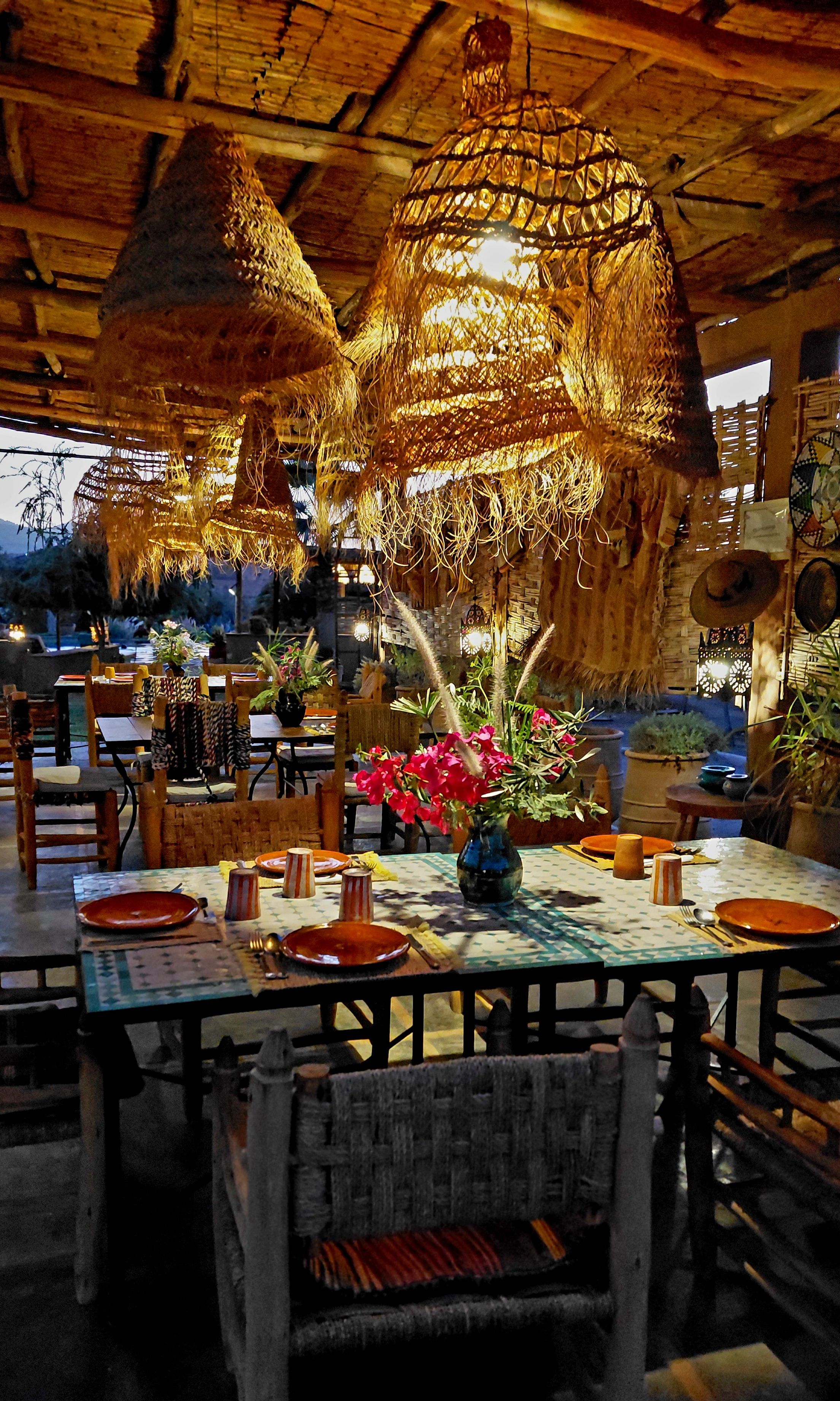 Een restaurant met rieten plafondlampen, houten tafels en stoelen.