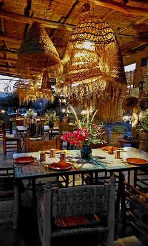 Un restaurant avec des lampes au plafond recouvertes de chaume, des tables et des chaises en bois.