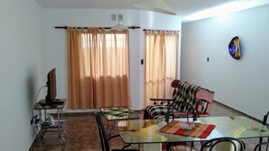 A dining area with a glass table, chairs, and a television on a stand.