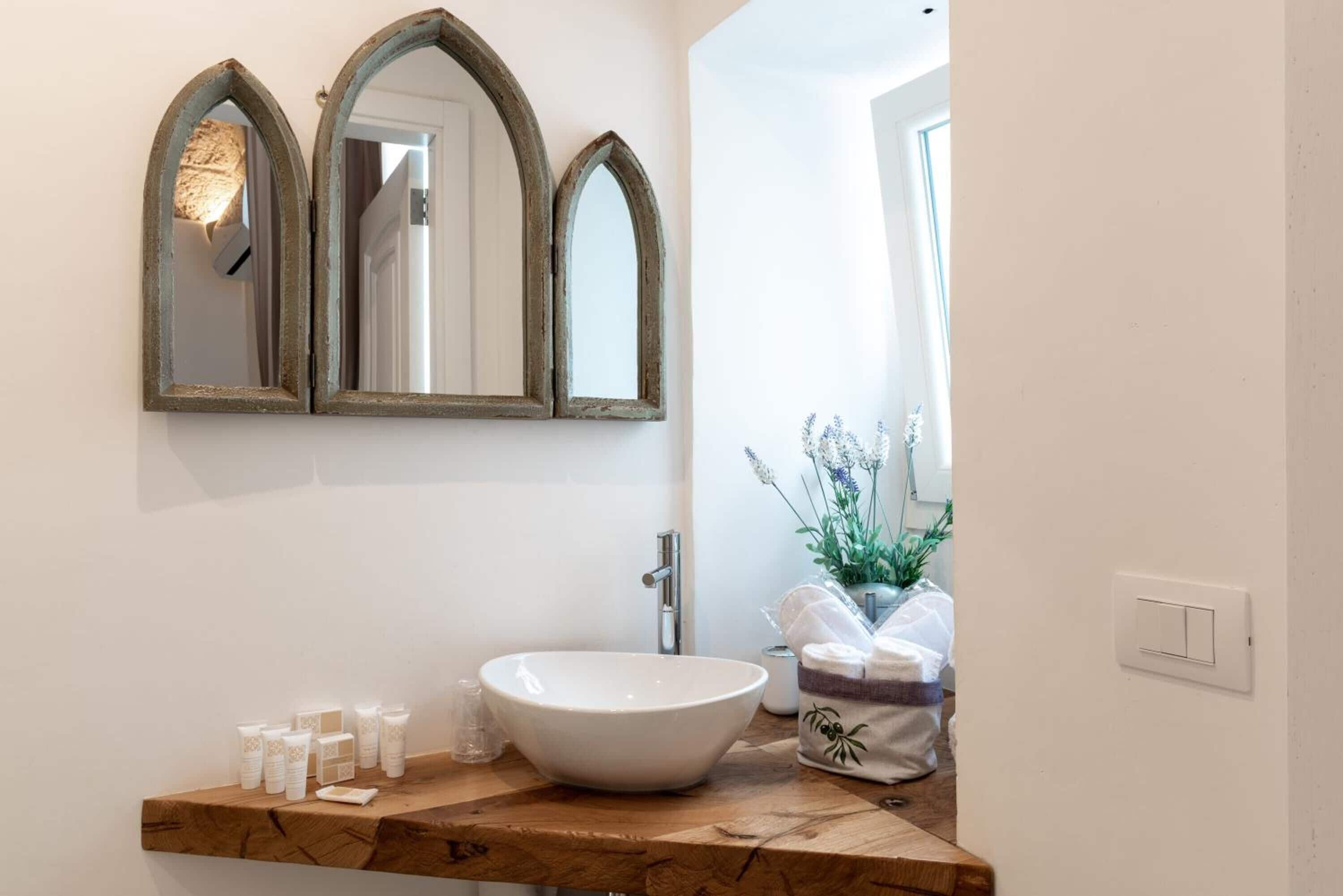 A bathroom with a wooden vanity, a white sink, and three arched mirrors.