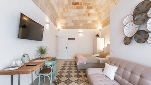 A cozy room with a checkered floor, a sofa, a TV mounted on the wall, and a dining area with a table and chairs. - D'aprile Dimore (Polignano a Mare)