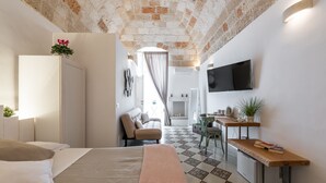 A modern bedroom with a brick ceiling, a bed, a desk, a TV, and a view of the living area. - D'aprile Dimore (Polignano a Mare)