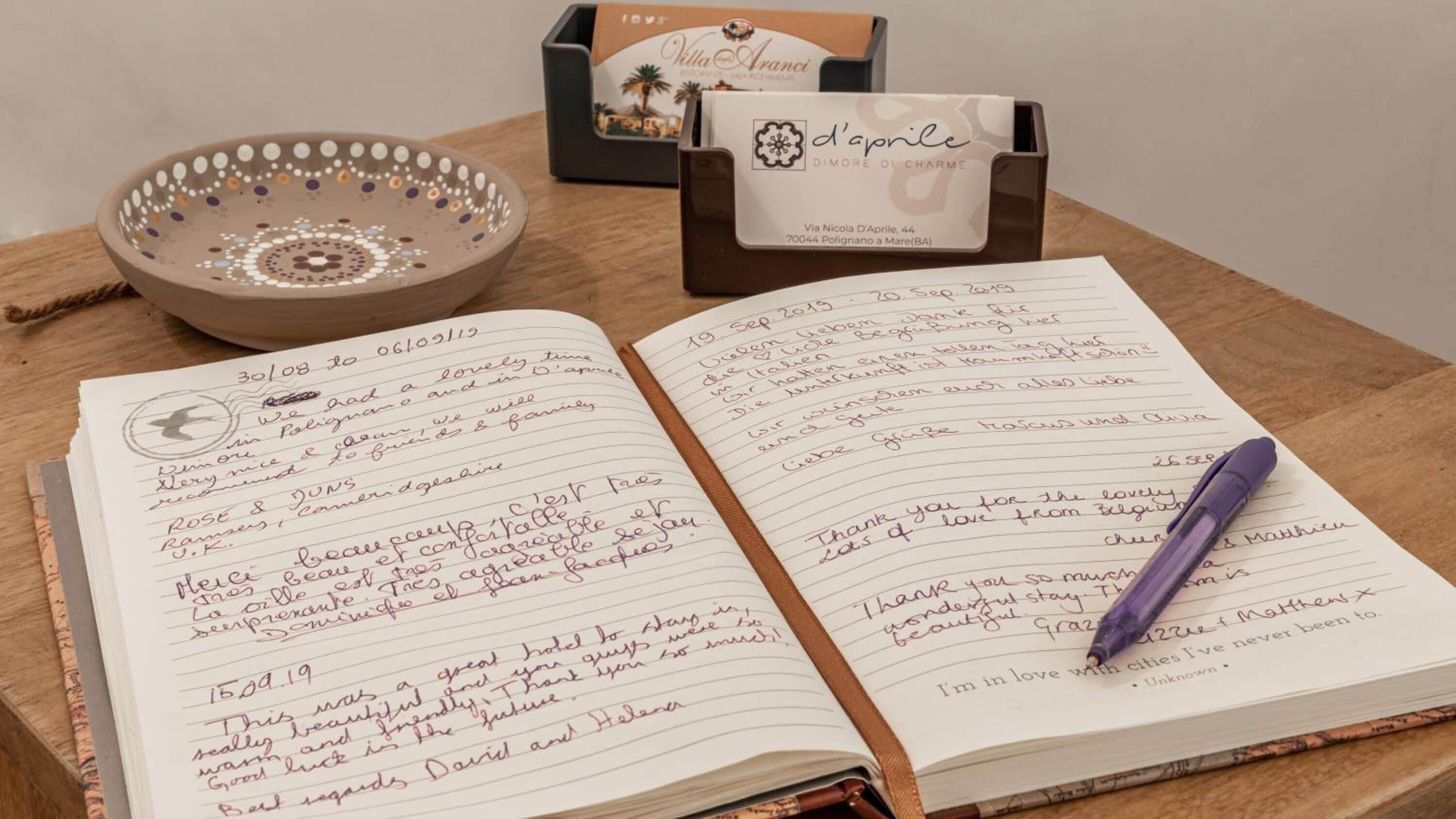 Un carnet rempli de notes manuscrites, un stylo violet et un bol décoratif sur une table en bois.