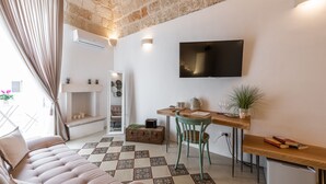 A cozy living room with a sofa, a dining table with chairs, a television mounted on the wall, and a fireplace. - D'aprile Dimore (Polignano a Mare)