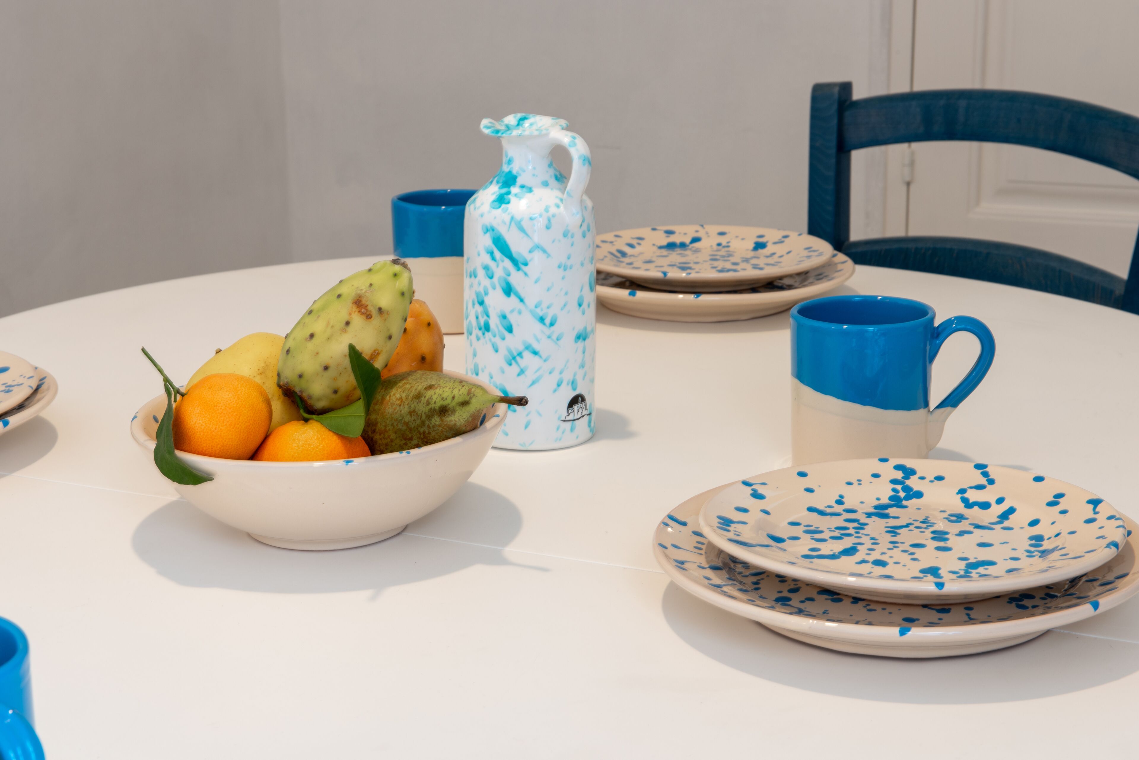 A dining table with a bowl of fruit, a pitcher, and blue and white plates.