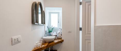 A bathroom with a wooden vanity, a white sink, and a mirror. There is a towel rack with folded towels and a small plant on the vanity.