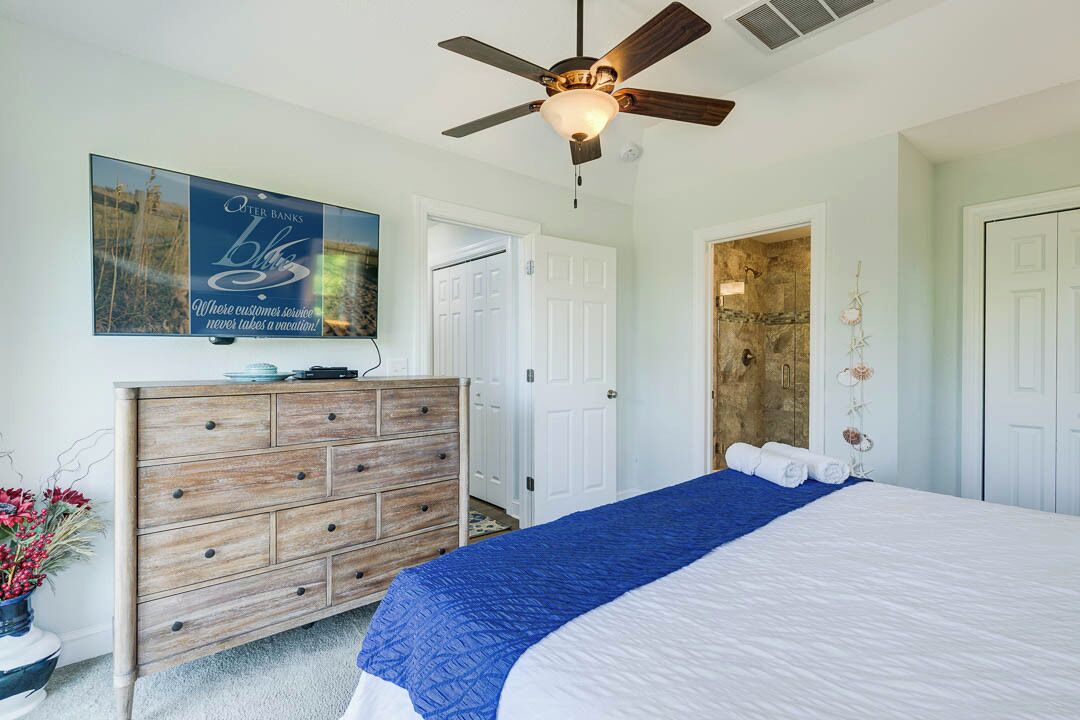 Ein Schlafzimmer mit einem Bett, einer Holzkommode, einem Deckenventilator und einem an der Wand montierten Fernseher.