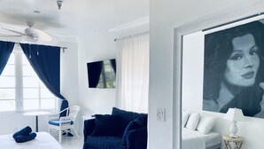 A hotel room with a bed, a blue sofa, a white armchair, a ceiling fan, a flat-screen TV, and a large mirror with a portrait. - Ocean view, luxury STUDIO, JACUZZI on Ocean drive (Miami Beach)