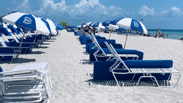 A beach with rows of blue and white beach chairs and umbrellas, a lifeguard tower, and the ocean in the background. - Ocean view, luxury STUDIO, JACUZZI on Ocean drive (Miami Beach)