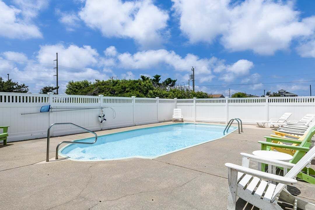 A rectangular pool with a white fence, lounge chairs, and a clear blue sky.