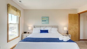 Hotelkamer met een groot bed, een raam met gordijnen, een nachtkastje met een lamp en een bord aan de muur.