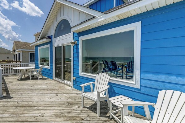 A blue building with a wooden deck, white chairs, and a table.