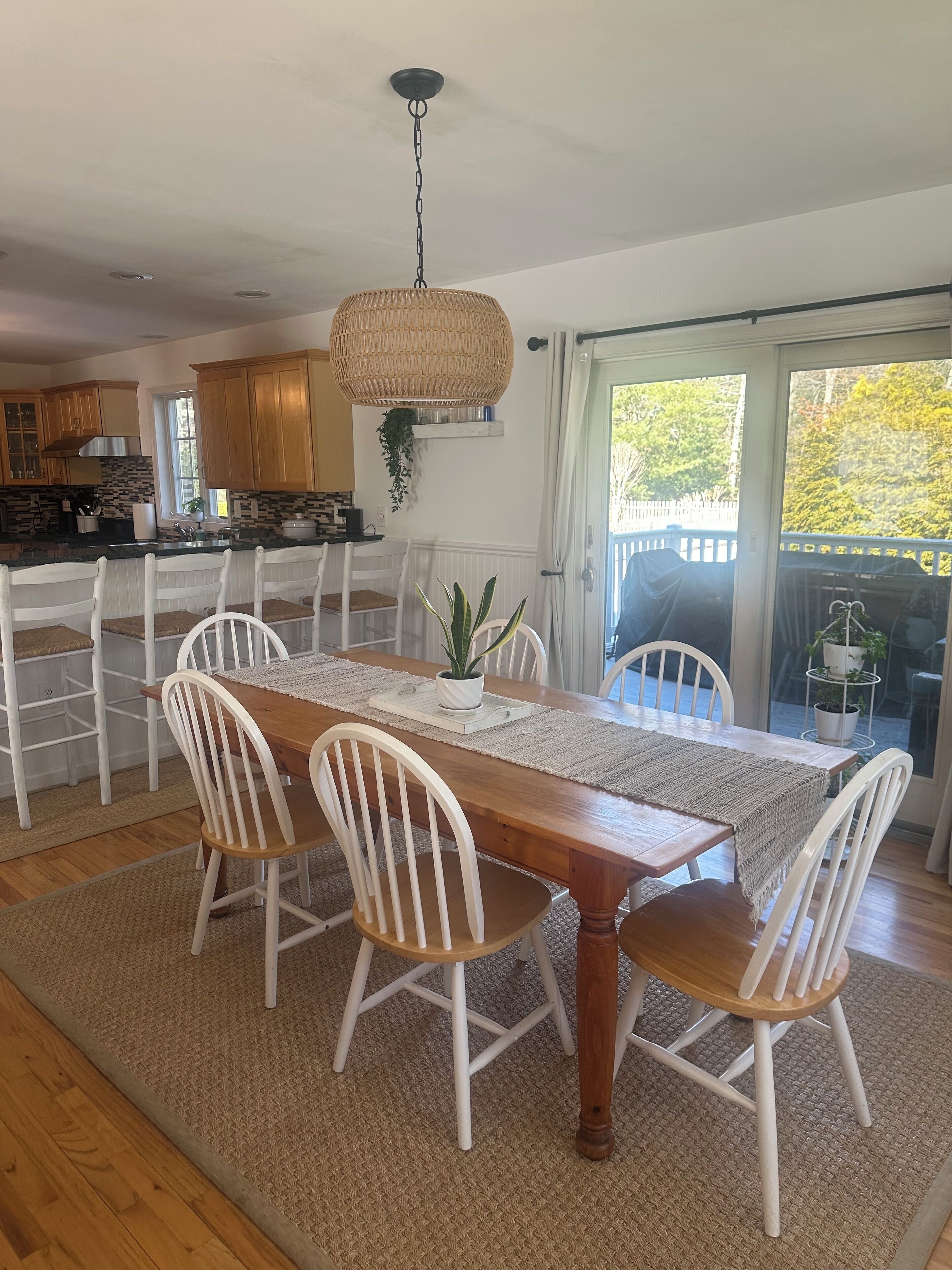 A dining area with a wooden table, white chairs, and a woven ceiling light fixture.