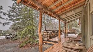 Een houten terras met Adirondack-stoelen, een overdekte veranda en uitzicht op een bebost gebied.