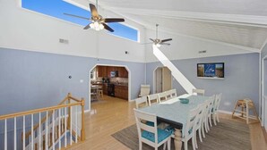A spacious dining area with a high ceiling and two ceiling fans, a kitchen in the background, and a staircase leading to an upper level. - Sandpiper Crossing | 555 ft from the beach | Private Pool, Hot Tub (Virginia Beach)