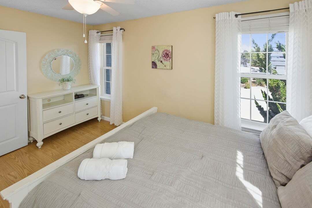 A bedroom with a bed, a dresser, a mirror, and a window with curtains.