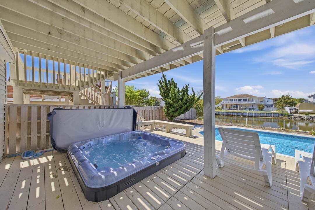 Ein Whirlpool auf einer Holzterrasse mit Blick auf ein Schwimmbecken und ein Haus im Hintergrund.