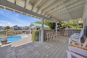 Um deck coberto ao ar livre com piscina, espaço para sentar e vista para casas através da água.