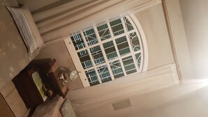 Une pièce avec une fenêtre, un ventilateur de plafond, une lampe et un tableau encadré au mur.