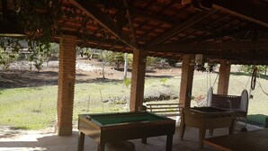 Un espace extérieur abrité comprenant une table de billard, des sièges et une vue sur un champ verdoyant.