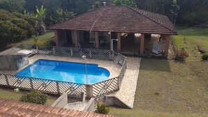 Une maison avec une piscine, entourée d’une terrasse en pierre et d’une clôture en bois.