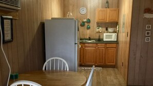 A compact kitchen with wooden cabinets, a refrigerator, a microwave, and a dining table with chairs. - BayShore Lodge 123 – Yellow Cabin #2 in Port O’Connor, TX
Prop ID:7580493 (Port O'Connor)