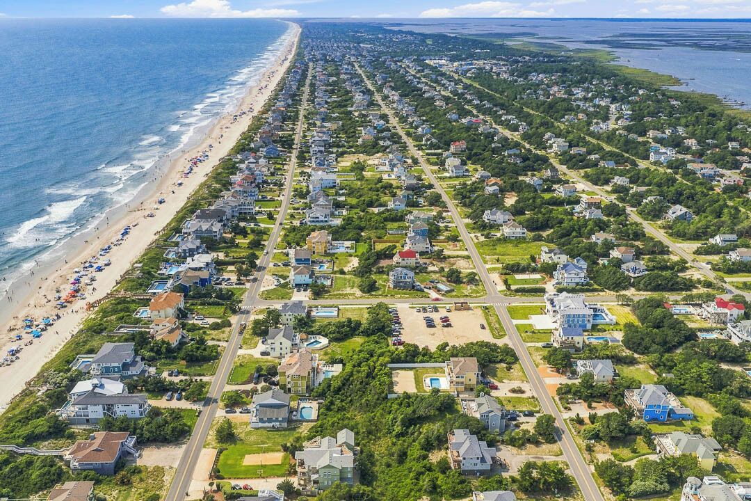 An aerial view of a coastal residential area with houses, a beach, and a road.
