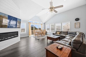 A spacious living room with a fireplace, a ceiling fan, and a large window.