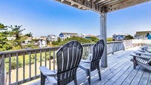 A wooden deck with Adirondack chairs, overlooking a residential area with houses and a clear blue sky. - Pelican Pointe | 355 ft from the Beach | Private Pool, Hot Tub | Corolla (Corolla)