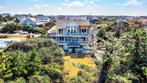 A large, two-story house with a prominent balcony and a small front yard. - Pelican Pointe | 355 ft from the Beach | Private Pool, Hot Tub | Corolla (Corolla)