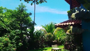 A garden with a pathway leading to a wooden bench, surrounded by lush greenery and a building with a tiled roof.