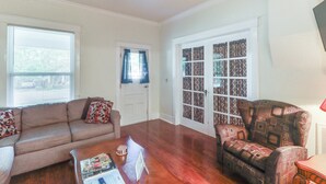 Uma sala de estar com um sofá de couro marrom, uma poltrona estampada, uma mesa de centro de madeira e um ventilador de teto.