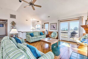 Relax in this inviting living room with a high ceiling, ceiling fan, and large window offering a view of the outside.