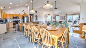 A spacious kitchen with wooden cabinets, a dining area with a large wooden table and chairs, and a view of the outside through large windows. - Sea Song II | 470 ft from the Beach | Private Pool, Hot Tub | Nags Head (Nags Head)