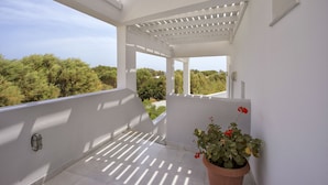 Un balcón blanco con una pérgola, una maceta con flores rojas y vistas a la vegetación.