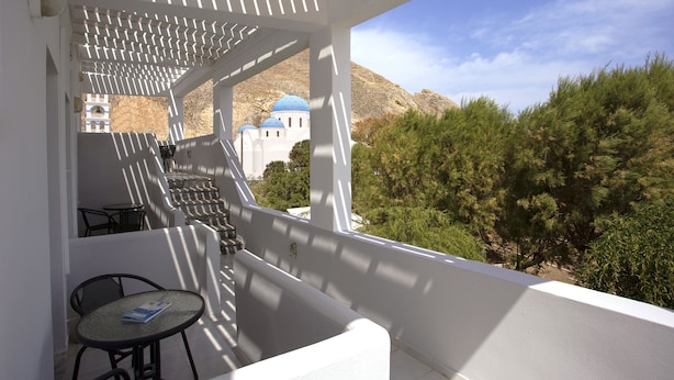 Un balcón con mesa y sillas, con vistas a un edificio de cúpulas azules y un paisaje montañoso.