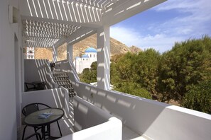 A balcony with a table and chairs, overlooking a building with blue domes and a mountainous landscape. - Sunrise Studios in Perissa (Santorini)